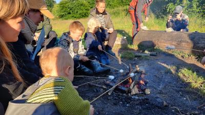Familiespejdere bager skumfiduser på bål i solnedgang